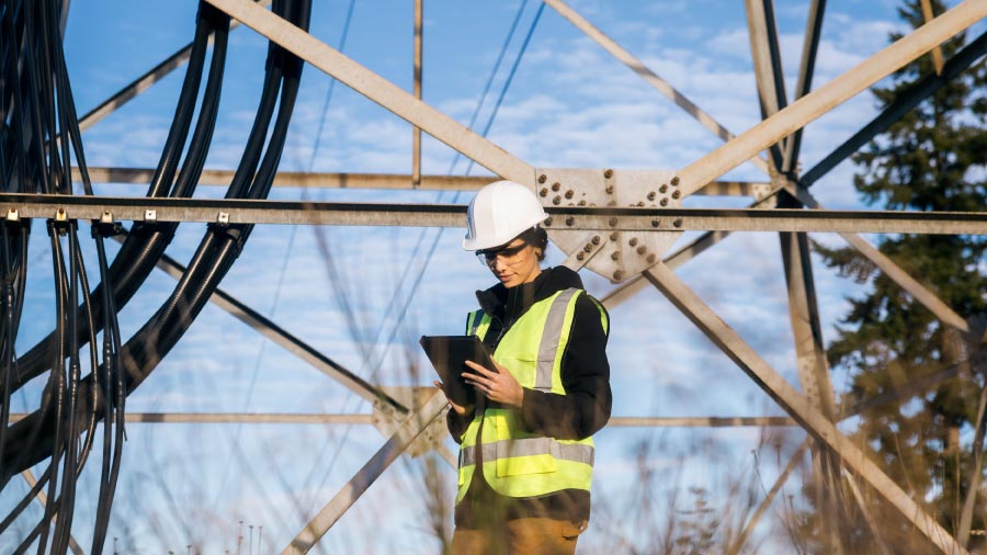 Electrical Utility Worker Performing Inspection Under High Voltage Tower Using A Tablet. How The Fulcrum And Slalom Partnership Brings Ai To Utility Field Operations