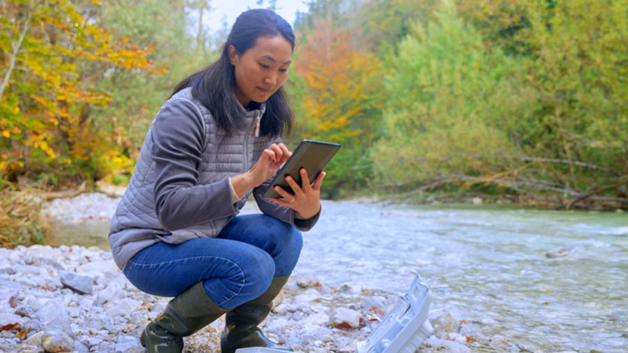 Female Biologist Using Digital Tablet While Testing Water Near River