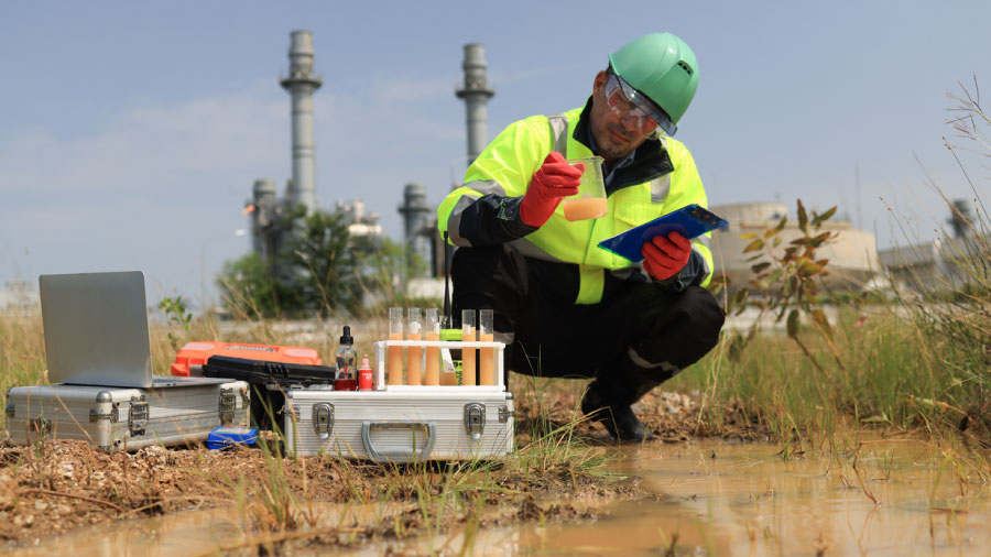 Technician Inspecting A Water Sample In A Beaker Beside Field Testing Equipment Outside An Industrial Facility Why Environmental Data Management Breaks Down Between Field And Office